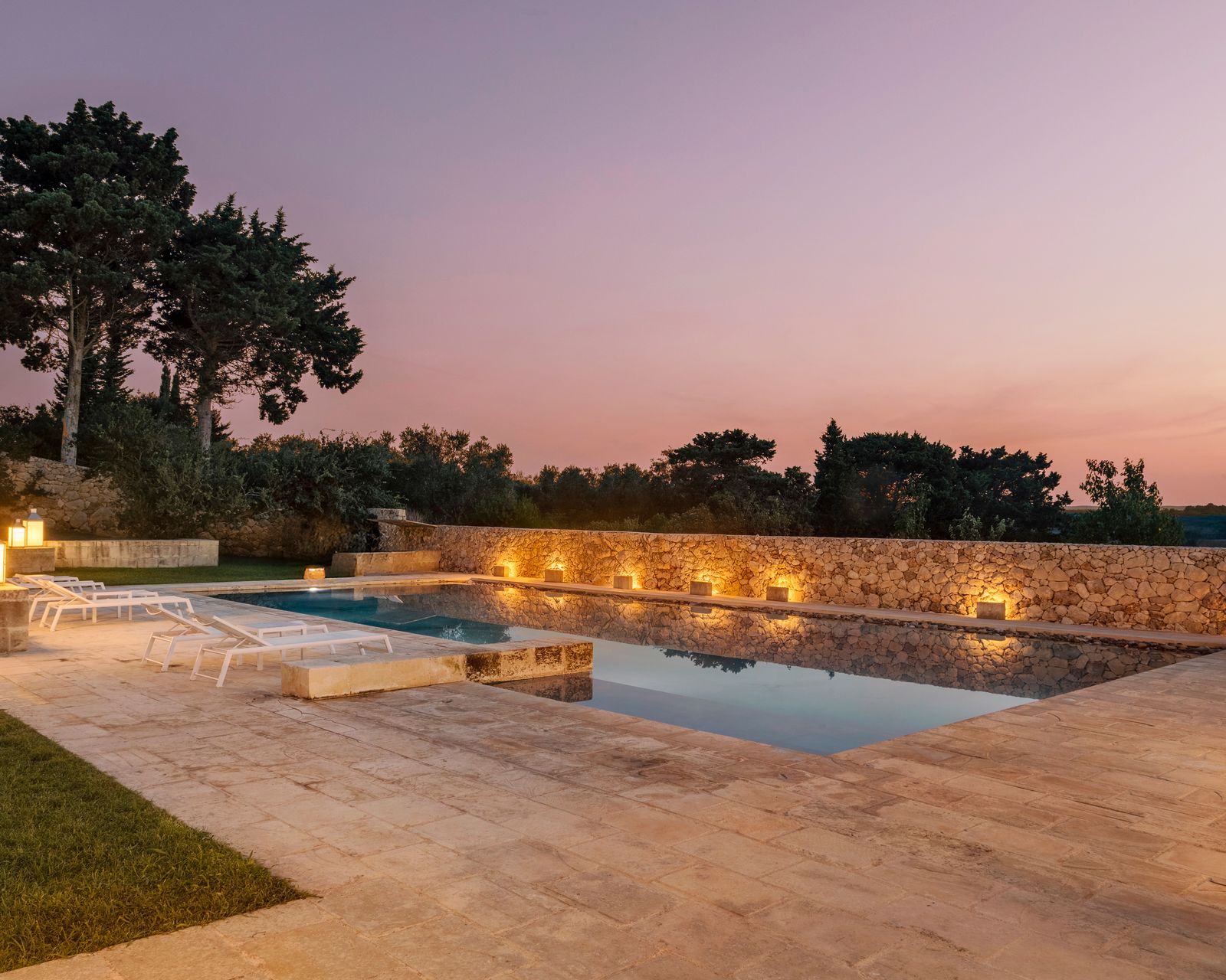 A masseria at dusk: the pool and the lit stone wall